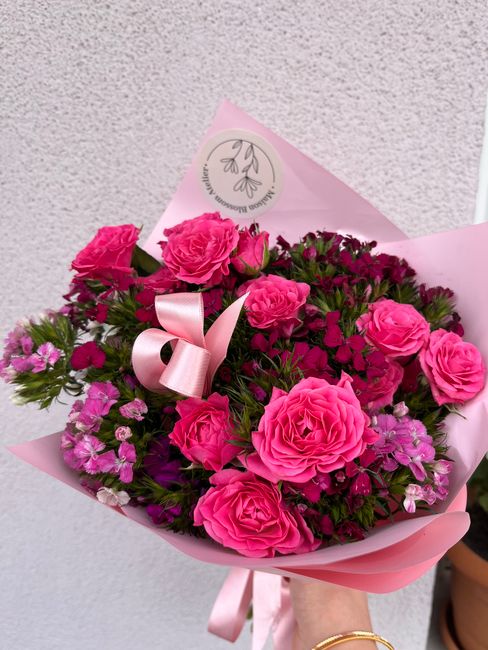 A vibrant bouquet of fresh pink roses and small purple flowers arranged in a rounded, lush cluster. The roses display fully opened petals with a soft, velvety texture and rich pink hues, while the sma